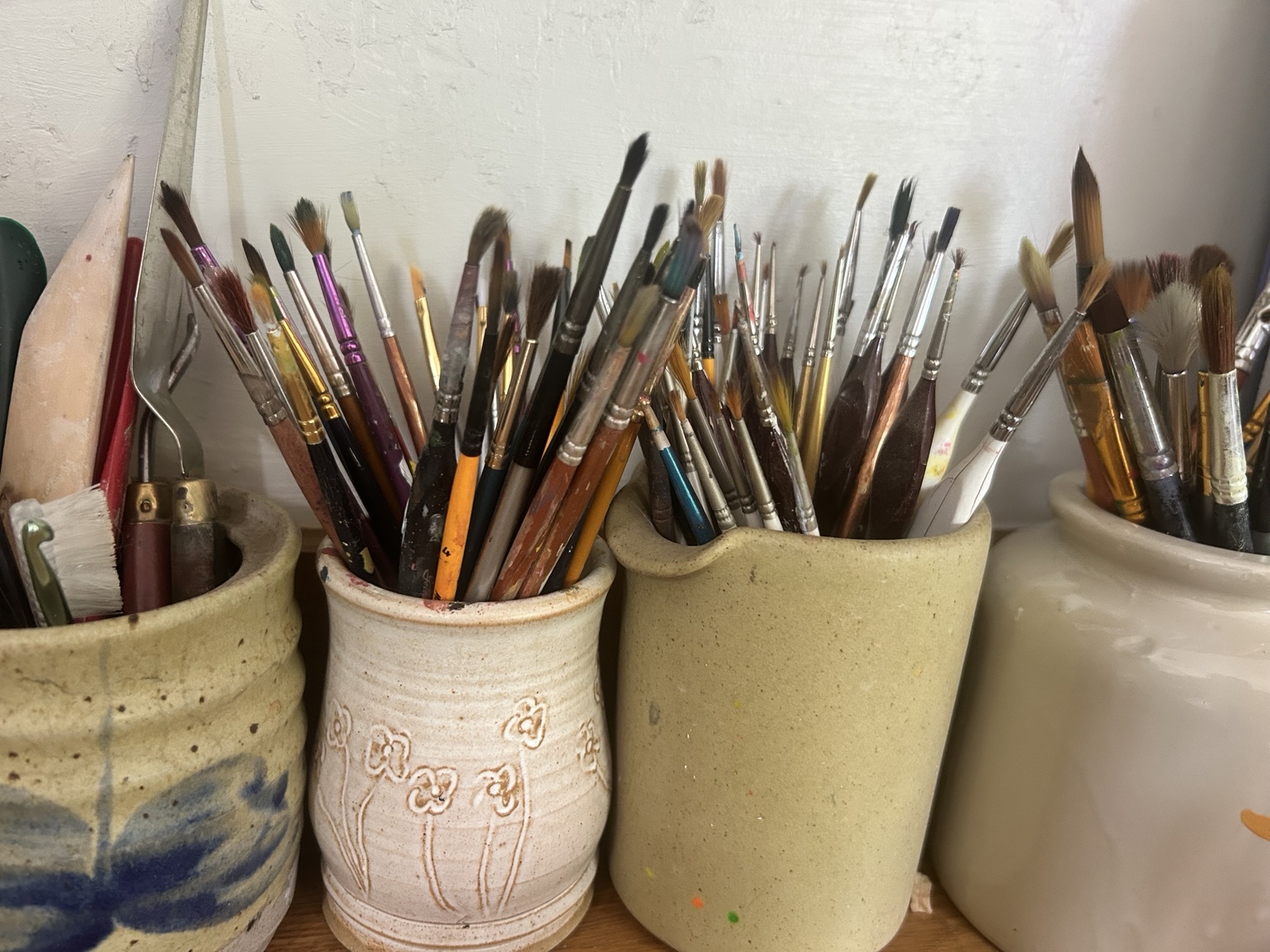 A collection of well-used paintbrushes held in handmade ceramic pots in Rebecca’s studio