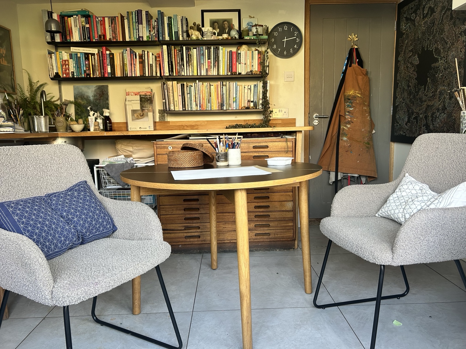 Two comfortable chairs facing one another in Rebecca’s studio, with books and art materials behind